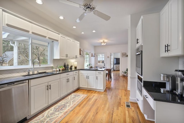 kitchen with dark countertops, visible vents, appliances with stainless steel finishes, a peninsula, and a sink