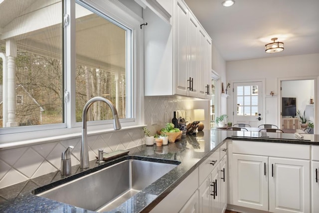 kitchen with a sink, backsplash, white cabinets, and dark stone countertops