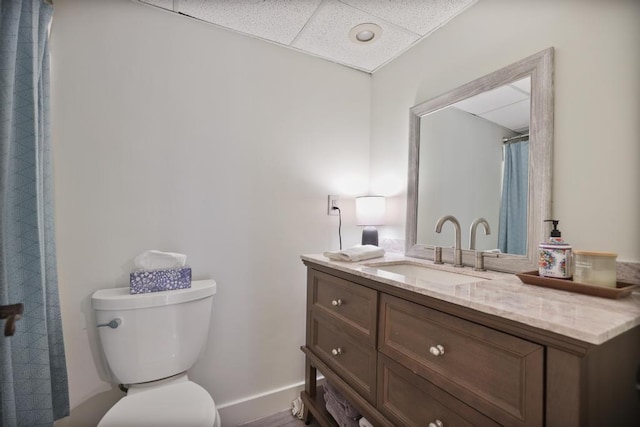 full bath featuring toilet, a shower with shower curtain, a paneled ceiling, baseboards, and vanity