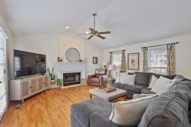 living room with visible vents, a fireplace with flush hearth, a ceiling fan, light wood finished floors, and vaulted ceiling