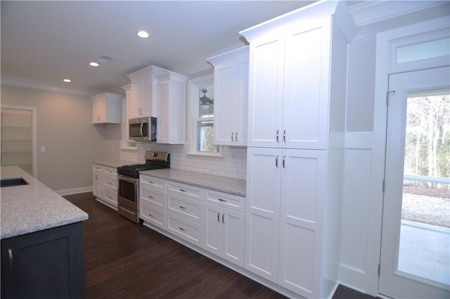 kitchen with white cabinets, backsplash, ornamental molding, dark wood-type flooring, and stainless steel appliances