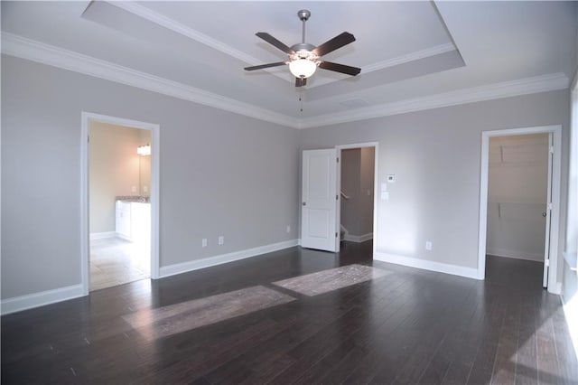 unfurnished bedroom with a spacious closet, a raised ceiling, ceiling fan, crown molding, and dark hardwood / wood-style floors