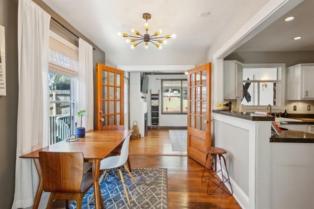 interior space featuring wood-type flooring, hanging light fixtures, french doors, white cabinets, and an inviting chandelier