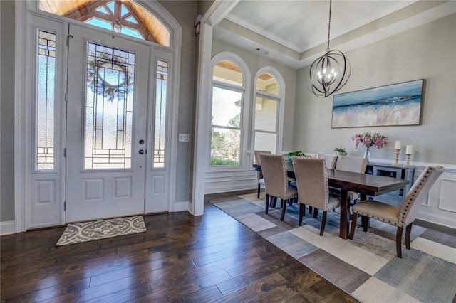 entryway featuring dark wood-type flooring, ornamental molding, a tray ceiling, a decorative wall, and a chandelier