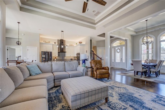 living area with visible vents, crown molding, ceiling fan with notable chandelier, wood finished floors, and a raised ceiling