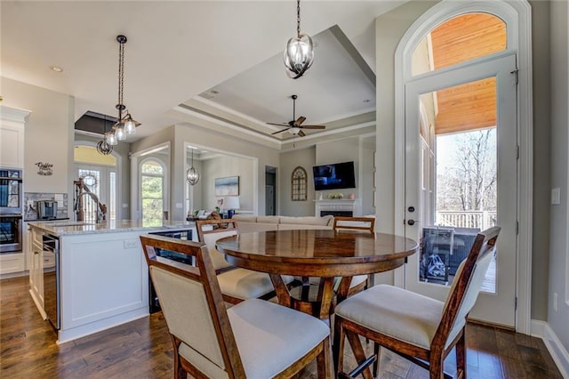 dining area featuring dark wood finished floors, a healthy amount of sunlight, a raised ceiling, and ceiling fan