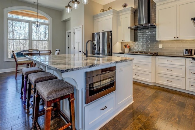 kitchen featuring backsplash, white cabinetry, appliances with stainless steel finishes, wall chimney range hood, and dark wood-style flooring