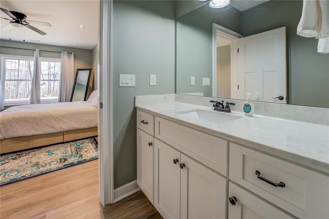 bathroom featuring a ceiling fan, wood finished floors, ensuite bath, baseboards, and vanity