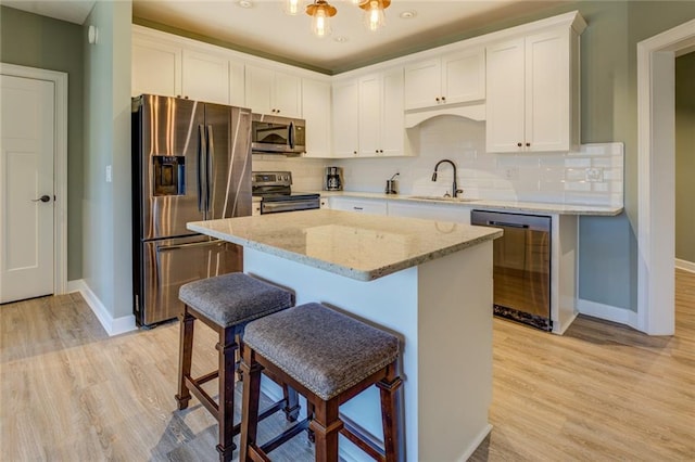 kitchen with a sink, light wood-style floors, tasteful backsplash, and appliances with stainless steel finishes