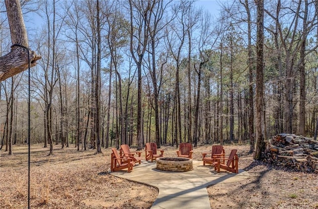 view of yard featuring a fire pit, a patio, and a view of trees