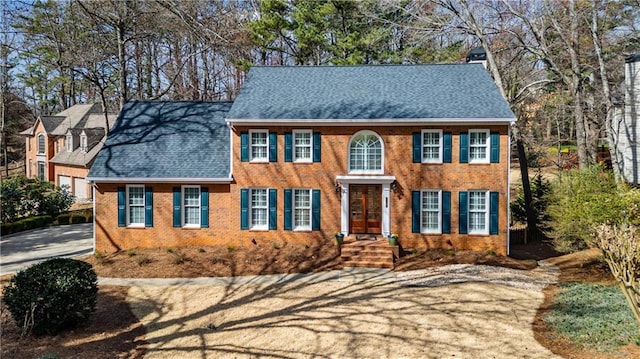 colonial-style house featuring brick siding and a shingled roof