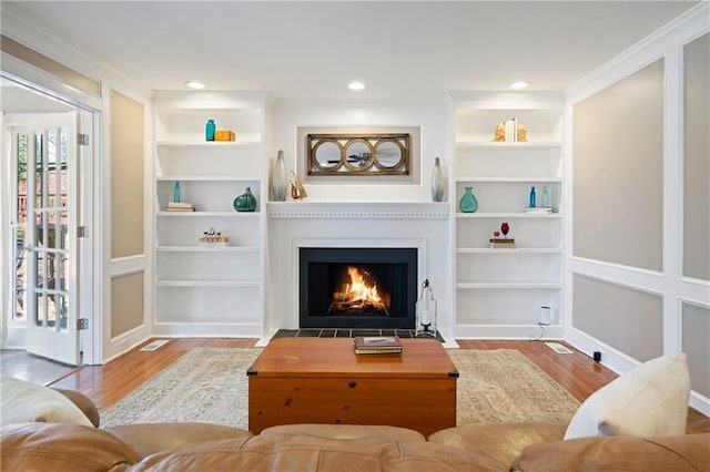 living area featuring built in features, wood finished floors, a fireplace, and ornamental molding