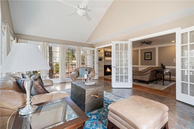 living area featuring a warm lit fireplace, french doors, high vaulted ceiling, and ceiling fan