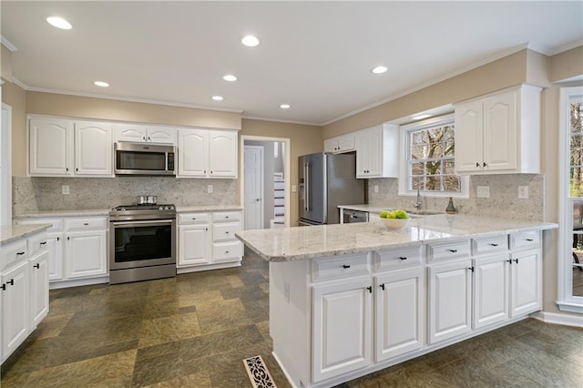 kitchen with a sink, light stone counters, white cabinetry, appliances with stainless steel finishes, and a peninsula