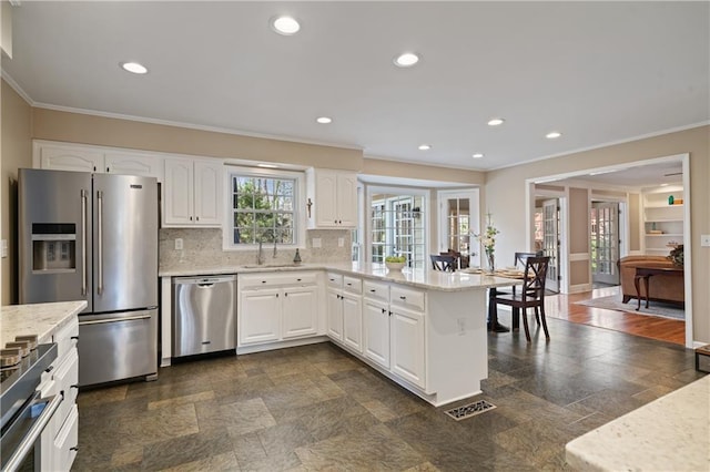 kitchen with backsplash, recessed lighting, appliances with stainless steel finishes, a peninsula, and a sink