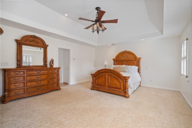 bedroom with light colored carpet, baseboards, a tray ceiling, and ceiling fan