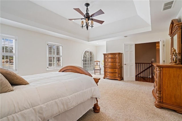 bedroom with a tray ceiling, multiple windows, light colored carpet, and visible vents