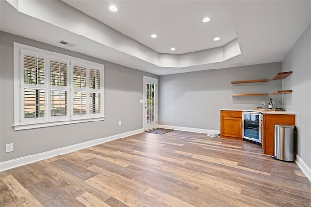 bar with a raised ceiling, light wood-style flooring, wine cooler, baseboards, and a dry bar