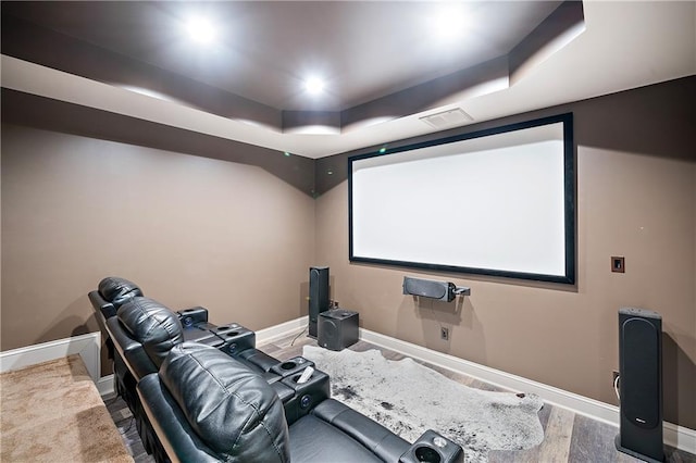 home theater with a tray ceiling, wood finished floors, visible vents, and baseboards