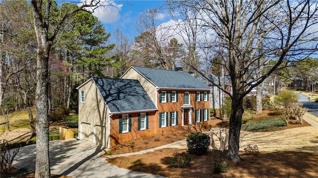 colonial-style house with concrete driveway, a garage, brick siding, and roof with shingles