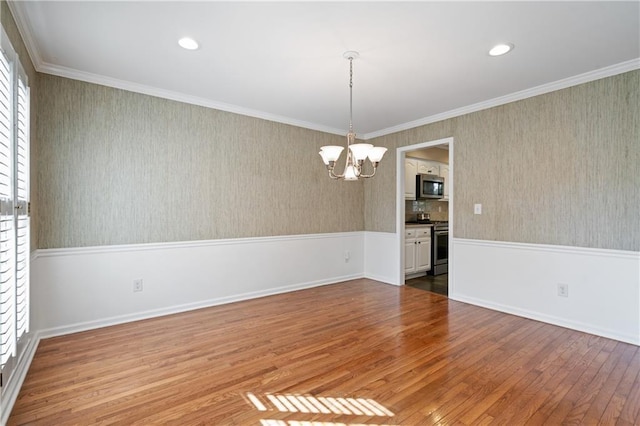 empty room featuring wallpapered walls, an inviting chandelier, wood-type flooring, wainscoting, and crown molding