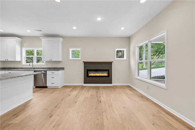 5232 W Mountain St, Stone Mountain, GA 30083 - kitchen featuring dishwasher, white cabinets, a glass covered fireplace, light wood finished floors, and dark stone counters