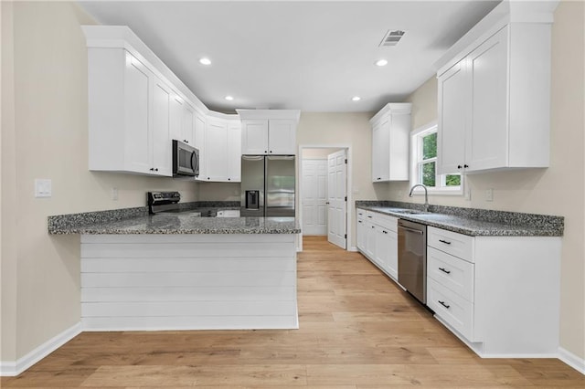 5232 W Mountain St, Stone Mountain, GA 30083 - kitchen with appliances with stainless steel finishes, a peninsula, light wood-style flooring, white cabinets, and dark stone counters