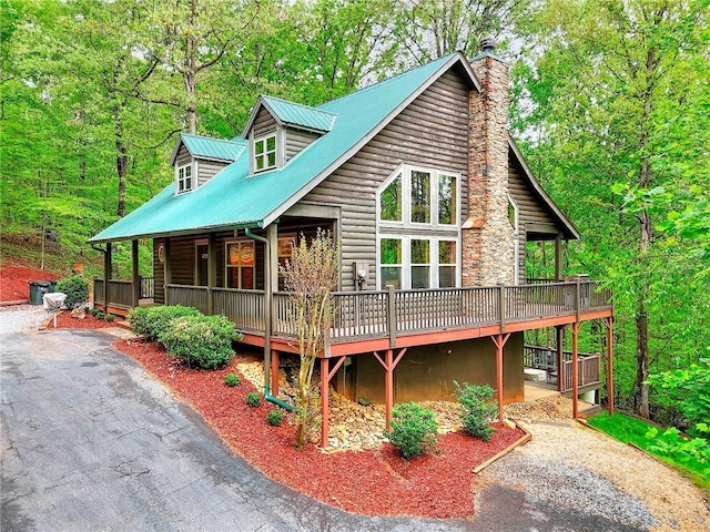 view of front of house with a wooden deck, faux log siding, metal roof, driveway, and a chimney