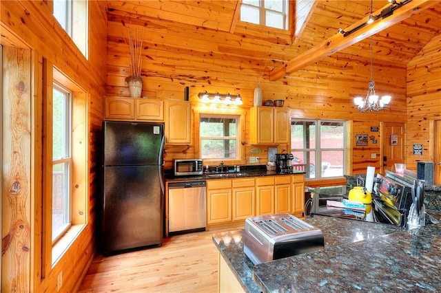 kitchen with appliances with stainless steel finishes, a wealth of natural light, wooden walls, and a sink