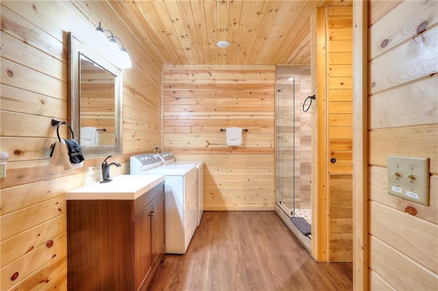 laundry area featuring wood ceiling, wooden walls, washer and dryer, light wood finished floors, and cabinet space