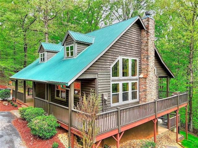 rear view of property with a chimney, aphalt driveway, log veneer siding, and metal roof