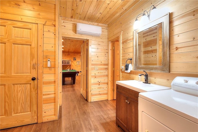 washroom with a sink, cabinet space, wood walls, washer / clothes dryer, and an AC wall unit