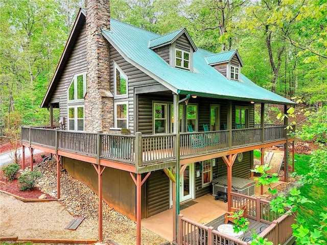 rear view of property featuring a chimney, metal roof, a deck, and faux log siding