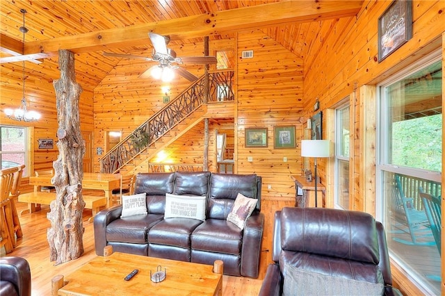 living room with stairs, beam ceiling, wooden walls, wood finished floors, and ceiling fan with notable chandelier