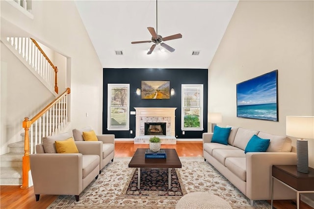 living room featuring light wood-type flooring, high vaulted ceiling, ceiling fan, and a stone fireplace