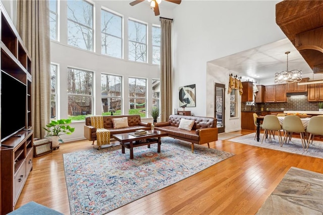 living room featuring ceiling fan with notable chandelier, a wealth of natural light, light hardwood / wood-style floors, and a towering ceiling