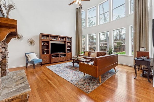 living room with ceiling fan, light hardwood / wood-style flooring, and a high ceiling