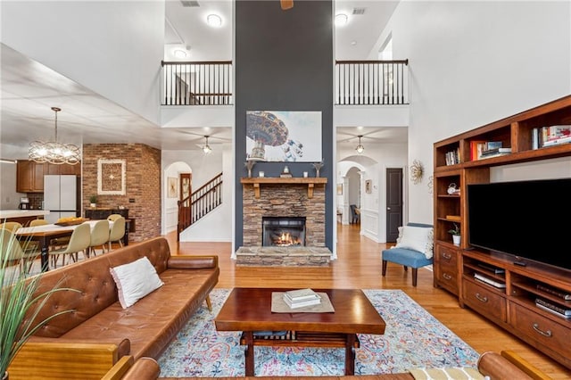 living room with a towering ceiling, ceiling fan with notable chandelier, a fireplace, and light hardwood / wood-style floors