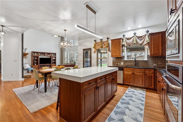 kitchen with sink, appliances with stainless steel finishes, decorative backsplash, a kitchen island, and decorative light fixtures