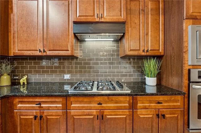 kitchen with wall chimney exhaust hood, appliances with stainless steel finishes, dark stone counters, and backsplash