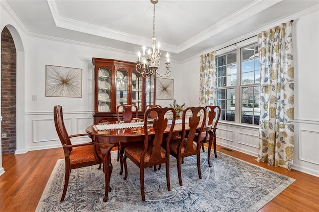 dining room featuring ornamental molding, hardwood / wood-style floors, a notable chandelier, and a tray ceiling