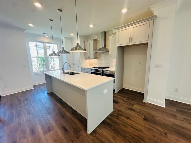 kitchen with an island with sink, wall chimney exhaust hood, sink, stainless steel range oven, and decorative light fixtures