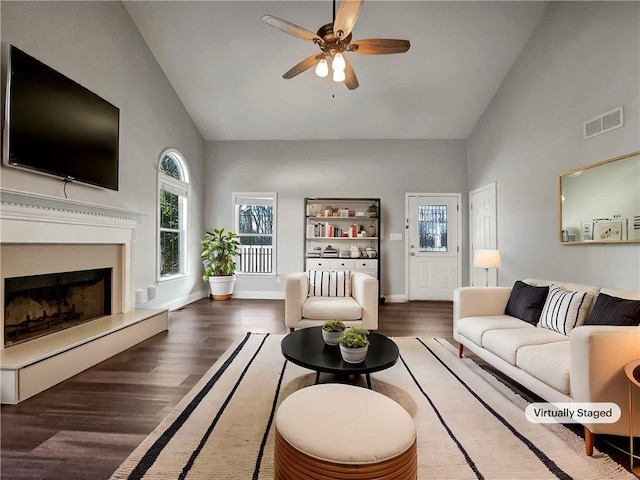 living area with visible vents, a fireplace with raised hearth, ceiling fan, wood finished floors, and high vaulted ceiling