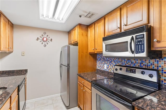 kitchen with dark stone countertops, decorative backsplash, light tile patterned flooring, and appliances with stainless steel finishes