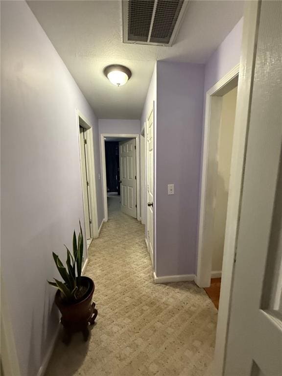 hallway featuring baseboards, visible vents, and light colored carpet