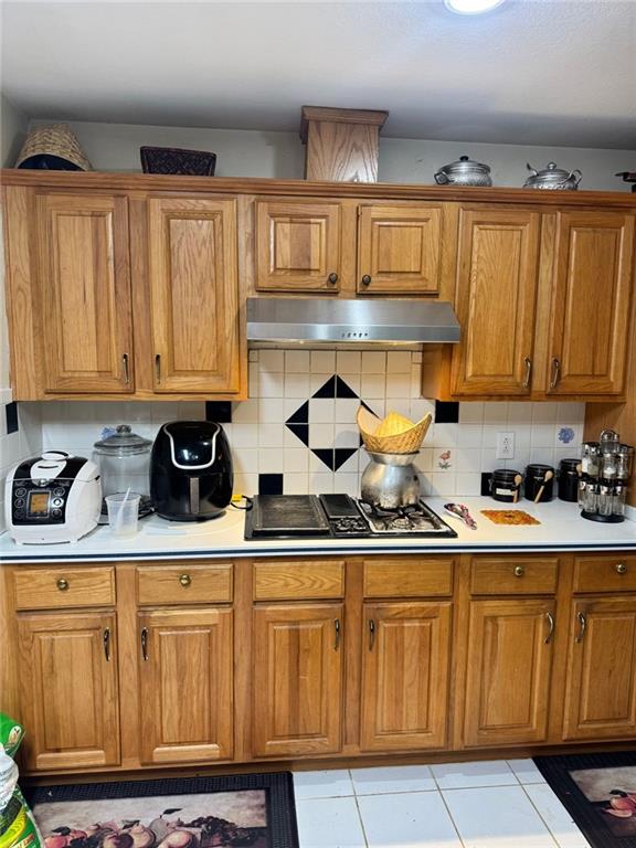 kitchen with decorative backsplash, under cabinet range hood, stovetop with downdraft, and brown cabinets