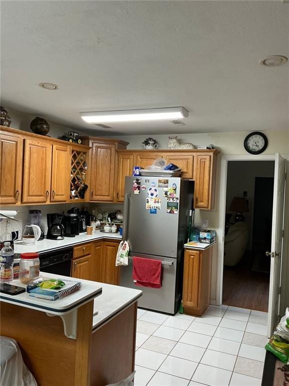 kitchen with light countertops, light tile patterned floors, freestanding refrigerator, a peninsula, and brown cabinetry