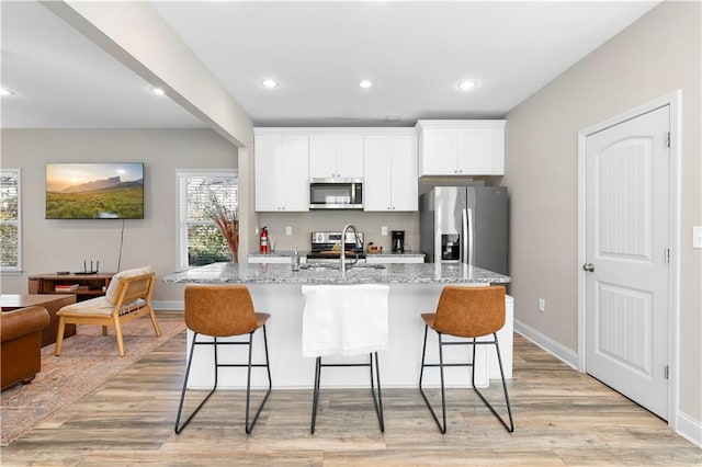 kitchen with white cabinetry, light stone countertops, stainless steel appliances, and a center island with sink