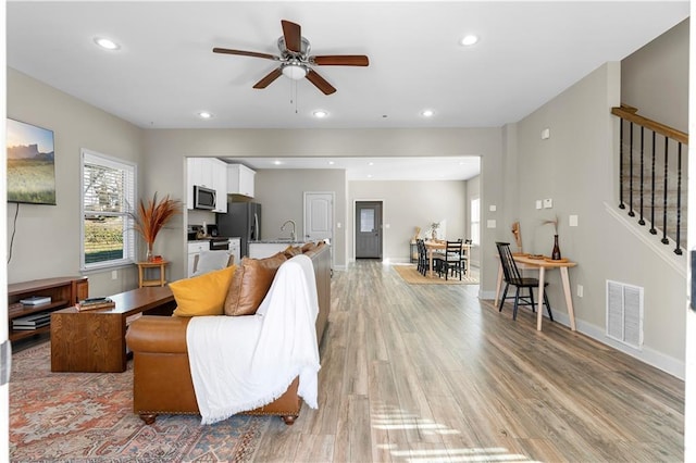 living room with ceiling fan, sink, and light wood-type flooring