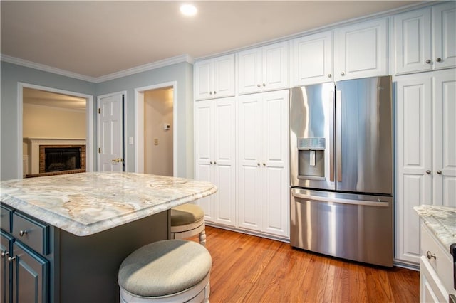 kitchen with a kitchen bar, white cabinetry, stainless steel fridge with ice dispenser, light hardwood / wood-style flooring, and crown molding